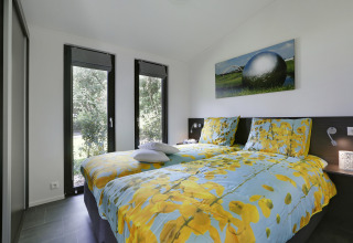 Slaapkamer in Bos Lodge van vakantiepark 't Schuttenbelt in Nederland met moderne stijl en grote ramen.