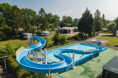 Glampingverblijf met blauwe waterglijbaan en zwembad, omringd door groene bomen, campers en hutjes.