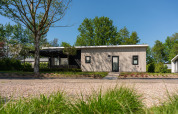 Moderne lodge ved feriestedet 't Schuttenbelt i Holland, omgivet af træer og frodig natur på solskinsdag.