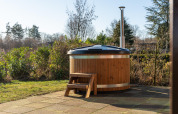 Buitenspa van hout met afdekking en trappetje op betegeld terras bij een lodge aan de tuin.