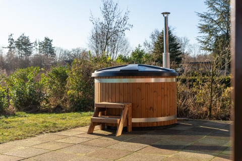 Bañera de hidromasaje de madera al aire libre con tapa y escalera en un patio junto a una cabaña.