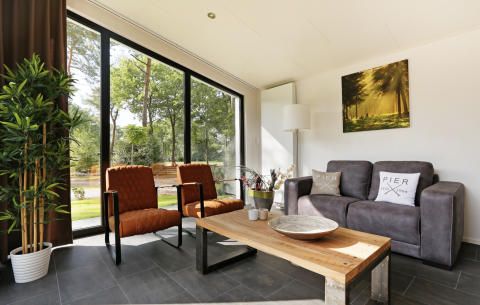 Modernes Wohnzimmer in der Forest Lodge mit großen Fenstern und Naturblick im Holiday Resort 't Schuttenbelt.