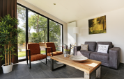 Moderne woonkamer met grote ramen, natuurzicht en comfortabel meubilair in Forest Lodge, Holiday Resort 't Schuttenbelt.