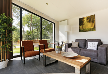 Salon moderne avec grandes fenêtres, vue sur la nature et canapé à Forest Lodge, Holiday Resort 't Schuttenbelt.