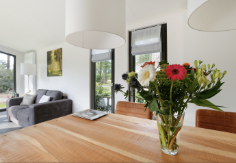 Bright lodge interior with flower bouquet on table, sofa and large windows, Forest lodge Netherlands.