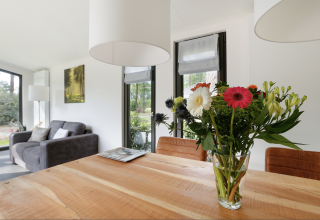 Licht lodge-interieur met bloemenboeket op tafel, bank en grote ramen, Forest lodge Nederland.