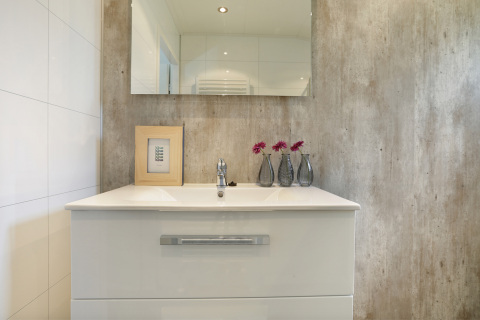 Modernes Badezimmer mit weißem Waschbecken, Spiegel, drei Vasen mit Blumen und gerahmtem Kunstwerk.