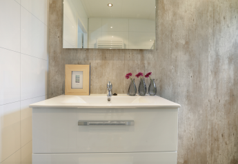 Modernes Badezimmer mit weißem Waschbecken, Spiegel, drei Vasen mit Blumen und gerahmtem Kunstwerk.
