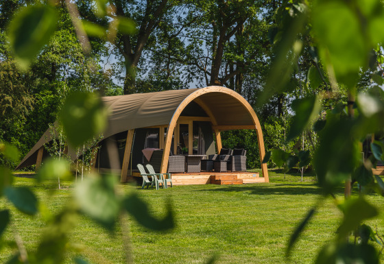 Stor safaritelthytte med terrasse og havemøbler på Holiday Resort 't Schuttenbelt i Holland omringet af natur.