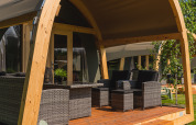 Überdachte Terrasse mit modernen Korbmöbeln vor einem Safari-Zelt im Holiday Resort 't Schuttenbelt, Niederlande.