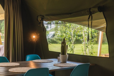 Innenansicht eines Safari-Zeltes mit Esstisch, Stühlen und Kaktus im Holiday Resort 't Schuttenbelt in den Niederlanden.