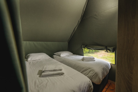 Zwei Einzelbetten mit weißer Bettwäsche in einem Safari-Zelt mit Fenster im Holiday Resort 't Schuttenbelt, Niederlande.