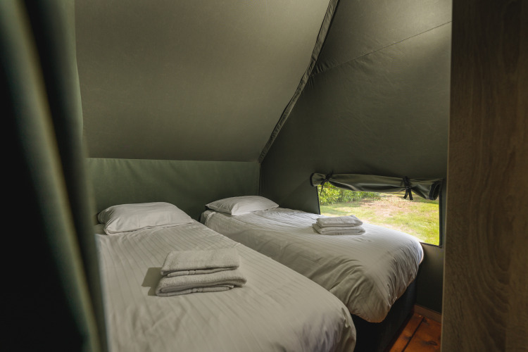 Twee eenpersoonsbedden met wit beddengoed in een safaritent met raam bij Holiday Resort 't Schuttenbelt, Nederland.