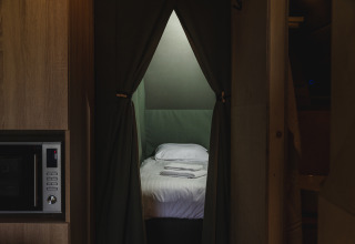 Vista interna di una tenda safari con letto, biancheria bianca e asciugamani presso Holiday Resort 't Schuttenbelt nei Paesi Bassi.