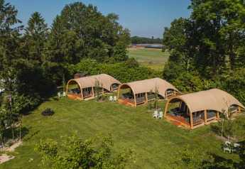 Vue aérienne de tentes safari au Holiday Resort 't Schuttenbelt, entourées d’arbres et de champs verts aux Pays-Bas.