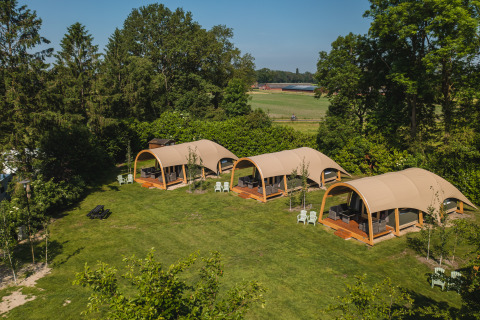 Aerial view of safari tents at Holiday Resort 't Schuttenbelt, surrounded by green trees and fields in the Netherlands.