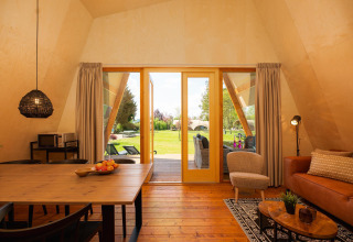 Interior view of a spacious safari tent lodge with modern décor, opening to lush green nature outside.