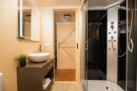 Baño moderno en tienda safari de lujo con ducha, lavabo, puerta corredera y espejo iluminado.