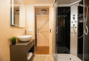 Modern bathroom in a luxury safari tent with shower, vessel sink, sliding barn door, and mirror.