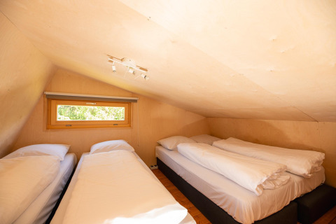 Dormitorio tipo loft en tienda safari con tres camas y techo bajo en Holiday Resort 't Schuttenbelt, Países Bajos.