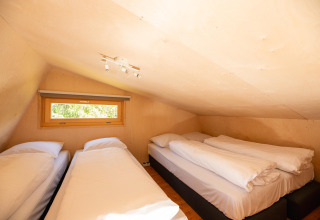 Dormitorio tipo loft en tienda safari con tres camas y techo bajo en Holiday Resort 't Schuttenbelt, Países Bajos.