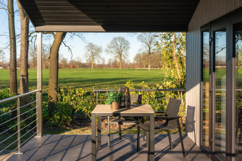Zonnig terras met tafel en stoelen bij Terrace Lodge met zicht op groene weiden in 't Schuttenbelt, Nederland.