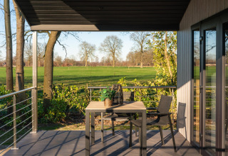 Terraza soleada con mesa y sillas en Terrace Lodge, con vistas a campos verdes en 't Schuttenbelt, Países Bajos.