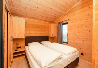 Schlafzimmer mit Doppelbett, Holzverkleidung und Fenster in der Terrace Lodge mit Sauna und Whirlpool, Niederlande.