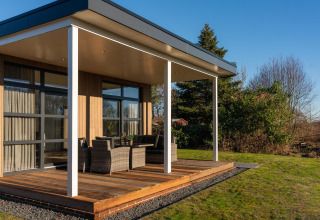 Moderne lodge met houten terras en buitenzitje bij Holiday Resort 't Schuttenbelt in Nederland.