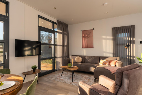 Moderne woonkamer in Vogellodge met veel lichtinval, zitbank en tv in Holiday Resort 't Schuttenbelt.