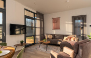 Sala moderna en Vogellodge con sofá acogedor, grandes ventanales y TV en Holiday Resort 't Schuttenbelt.