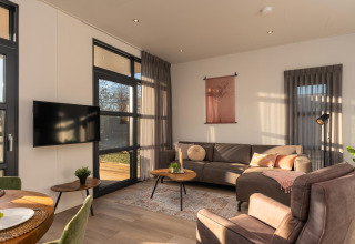 Moderne woonkamer in Vogellodge met veel lichtinval, zitbank en tv in Holiday Resort 't Schuttenbelt.