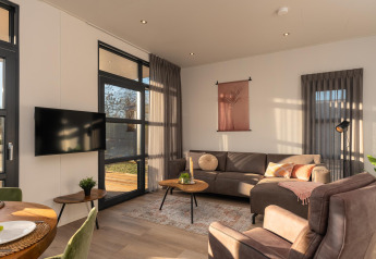 Moderne stue i Vogellodge med komfortable møbler, store vinduer og tv på Holiday Resort 't Schuttenbelt.