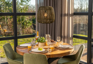 Mesa redonda de madera con desayuno y sillas verdes en una luminosa cabaña del resort 't Schuttenbelt.