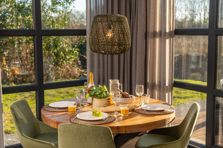 Mesa redonda de madera con desayuno y sillas verdes en una luminosa cabaña del resort 't Schuttenbelt.