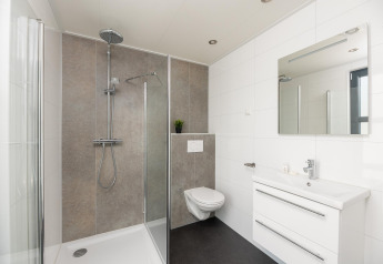 Moderne badkamer in Vogellodge met douche, zwevend toilet en wastafel in 't Schuttenbelt vakantiepark.