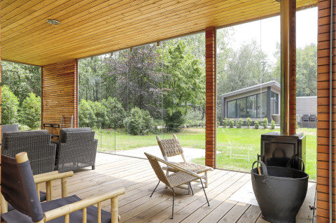 Overdækket terrasse med siddemøbler og udsigt til en grøn have og moderne bygning på Woody Lodge Florian.