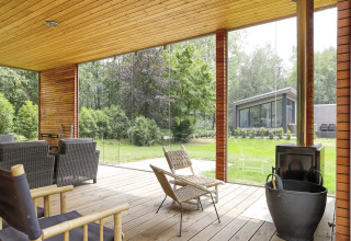 Terrasse couverte avec sièges en rotin et poêle à bois à Woody Lodge Florian, aux Pays-Bas.