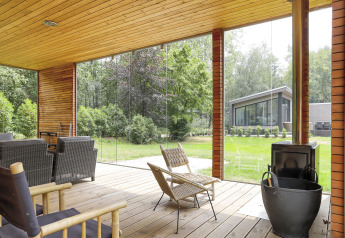 Overdekt terras met rotan stoelen, houtkachel en tuinzicht bij Woody Lodge Florian in Nederland.