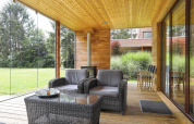 Moderne Terrasse mit Glaswänden, gemütlichen Rattanstühlen und Naturblick, Woody Lodge Florian, Niederlande.