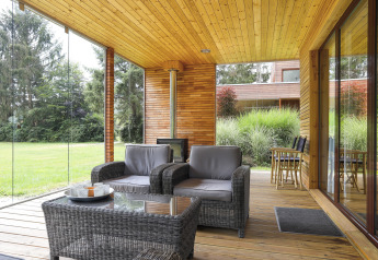 Patio moderno con pareti in vetro, poltrone in vimini e vista sul verde, Woody Lodge Florian, Paesi Bassi.