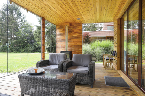 Modern patio with glass walls, wicker armchairs, wooden ceiling and scenic view, Woody Lodge Florian, Netherlands.