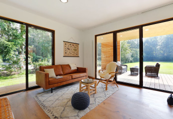 Lichte moderne woonkamer in Woody Lodge Florian met grote ramen en uitzicht op tuin en terras.