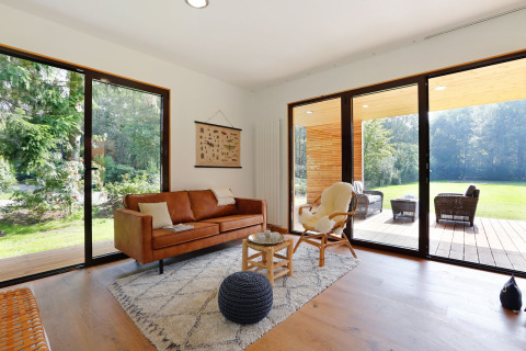 Lichte moderne woonkamer in Woody Lodge Florian met grote ramen en uitzicht op tuin en terras.