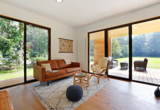 Lichte moderne woonkamer in Woody Lodge Florian met grote ramen en uitzicht op tuin en terras.