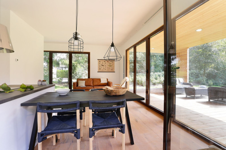 Modernes Wohnzimmer der Woody Lodge Florian mit Panoramafenstern, Holztisch und Blick ins Grüne.