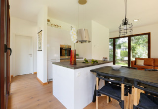 Moderne, lys lodgekøkken og spiseområde med store vinduer, trægulve og udsigt til grøn have i Holland.