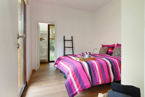 Dormitorio moderno con ropa de cama rosa a rayas, suelo de madera y acceso al baño en Woody Lodge Florian.