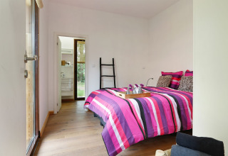 Dormitorio moderno con ropa de cama rosa a rayas, suelo de madera y acceso al baño en Woody Lodge Florian.