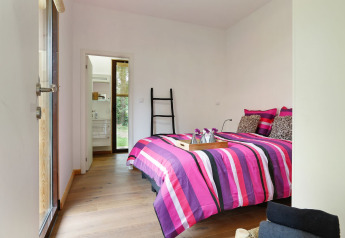 Dormitorio moderno con ropa de cama rosa a rayas, suelo de madera y acceso al baño en Woody Lodge Florian.